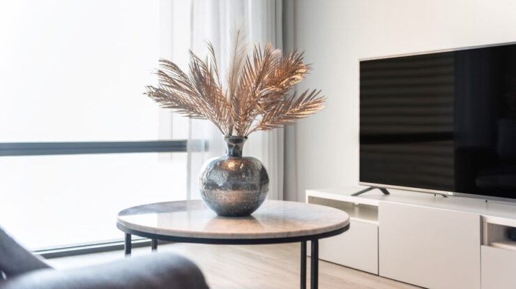 Stylish living room featuring a TV, table, and a vase with decorative leaves. - Photo by Louie Alma on Pexels